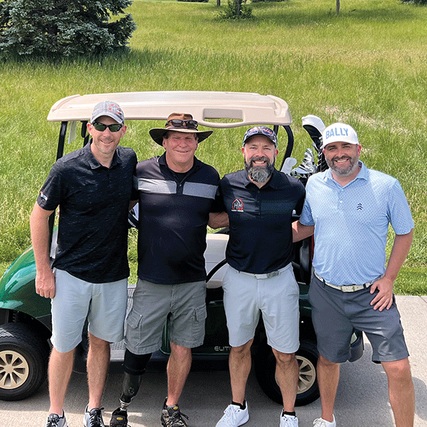 Four white men participating in Tee It Up for Sight, standing in front of a golf cart.