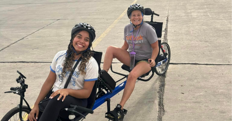 Two ladies smiling on a tandem bike ready to take off.