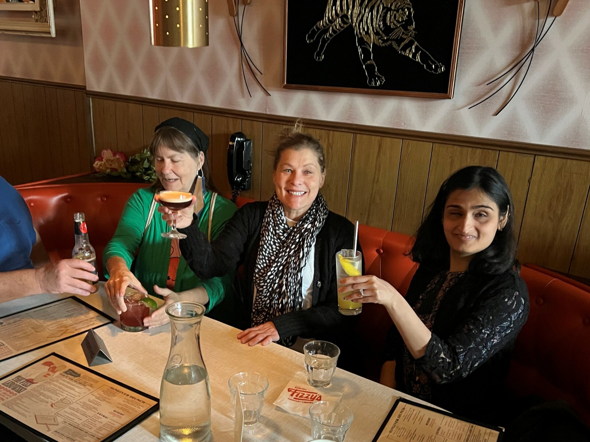 Three ladies at a table holding their drinks up for a cheers.