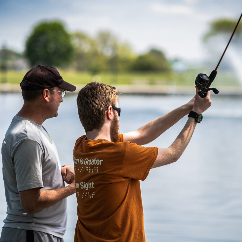 A man assisting an Enrichment consumer with casting his line.