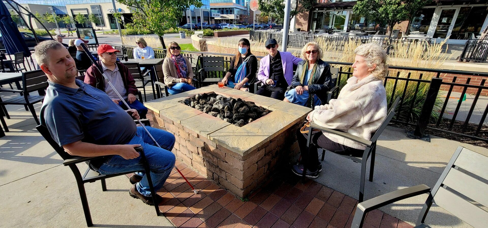 A group of 8-10 people sitting around a table outside. Some of them are holding their white canes. This is a picture from a previous year's White Cane Day Happy Hour at a bar in Aksarben.