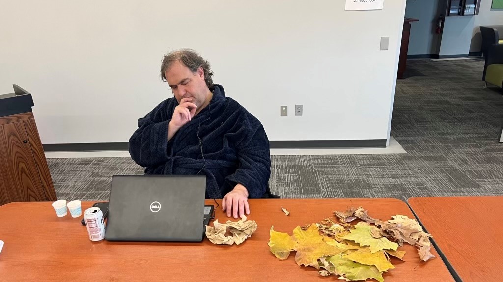 Ryan sitting at a table in a robe. His eyes are closed and his hand is cusping his chine. He looks to be in deep thought while listening the instructor reads a short story outloud.