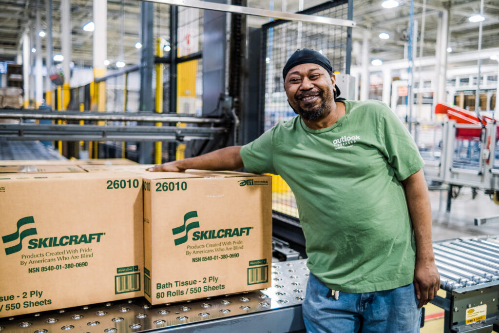 Alex Curtis smiles for the camera while leaning against a box of Skillcraft products.