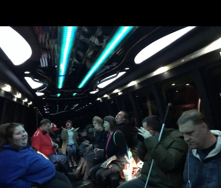 A group of adults in shuttle. The ceiling is lit up with rows of lights. The people in the picture all have their mouths open like they are probably singling a Christmas Carol.