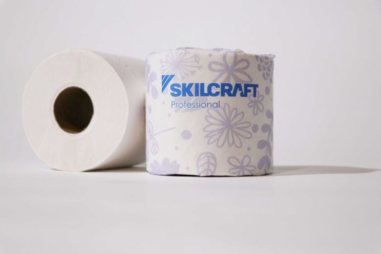 Two rolls of toilet paper sit side by side. One is wrapped in Skillcraft paper