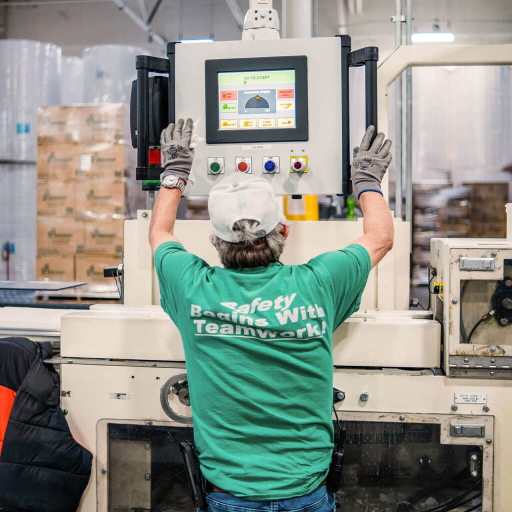 A man in a green shirt looks at a computer screen on production equipment