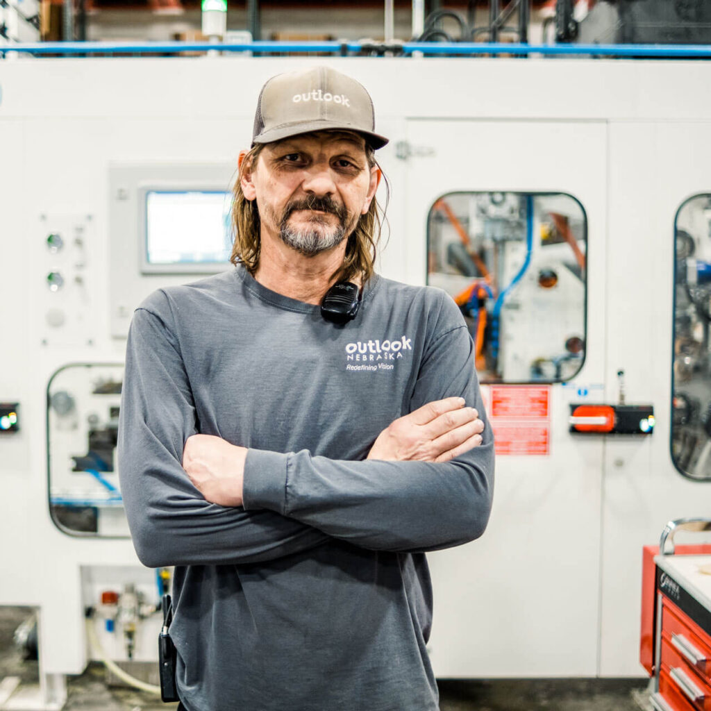 A man stands with his arms crossed in front of production equipment