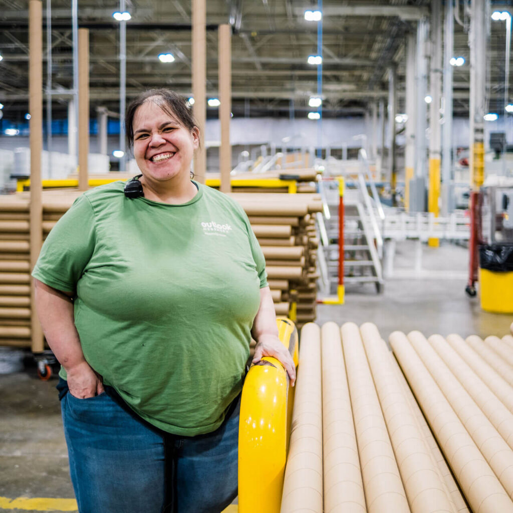 A woman in a green shirt smiles while standing in the Outlook Nebraska warehouse