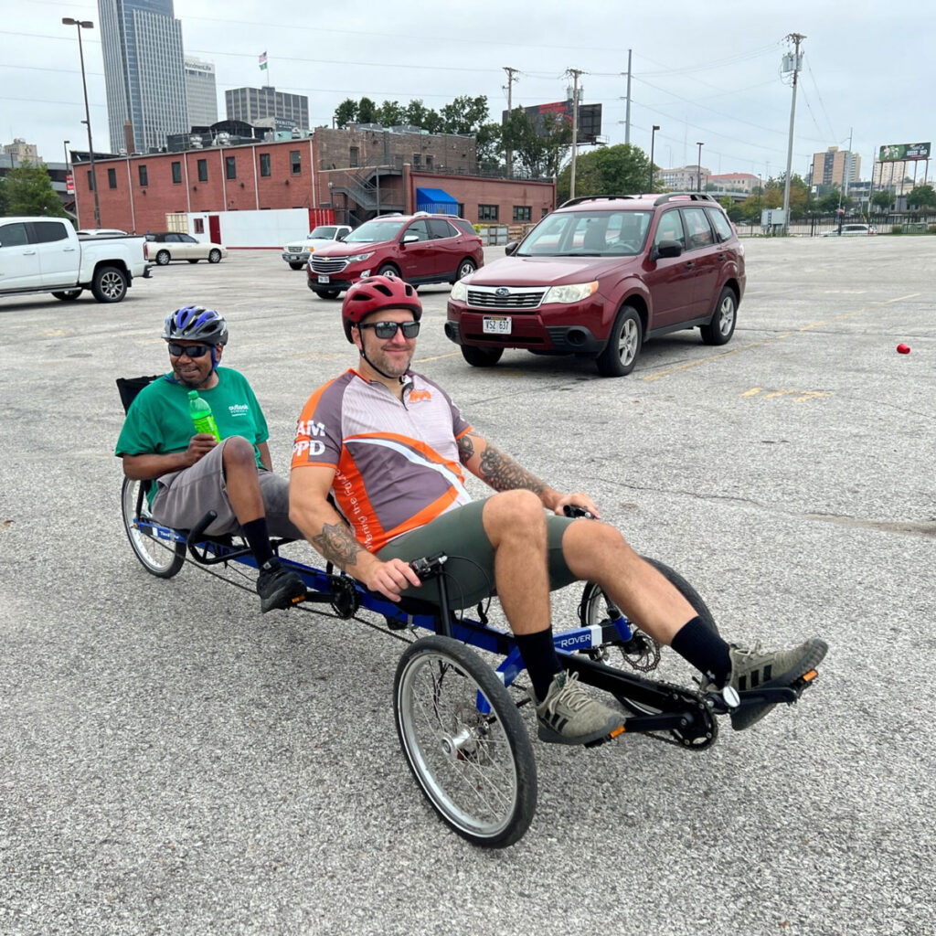 Two men on a recumbent tandem bike wearing helmets. They are getting ready to start pedaling away.