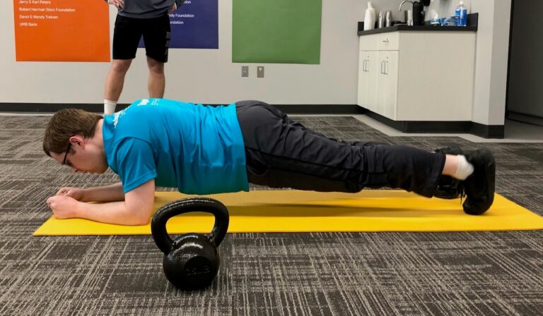 A man planking on a yoga mat. There is a kettle bell in view also.