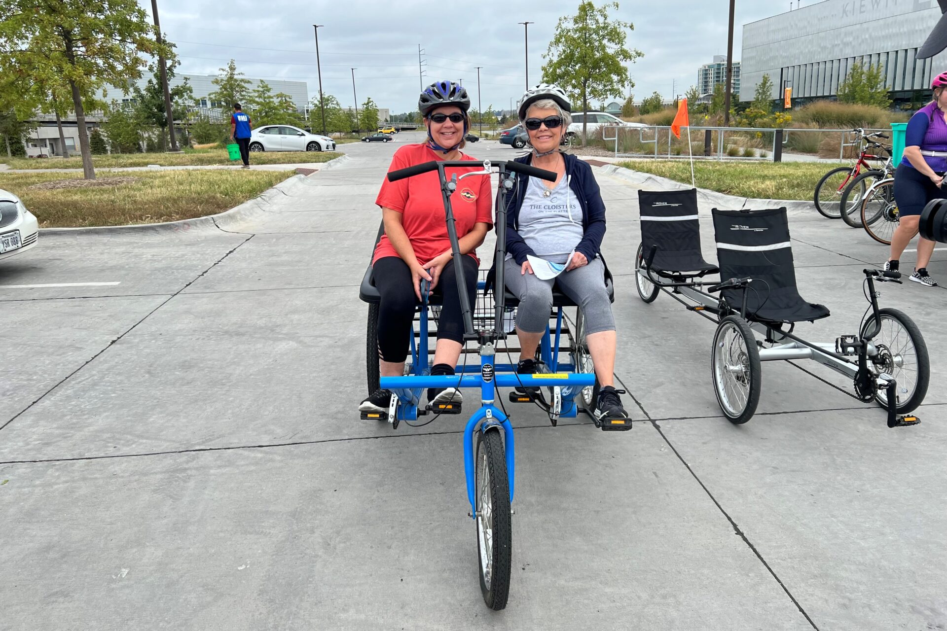 Two ladies wearing, smiling, seated side by side on a recumbent tandem bike