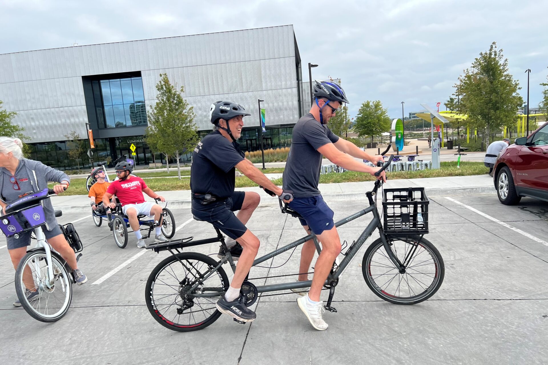 side view of 2 people riding on a tandem bike.