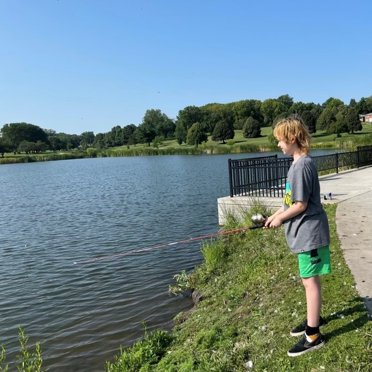 the view of teenage boy from the side with a lake in the background. He is casting a fishing pole.