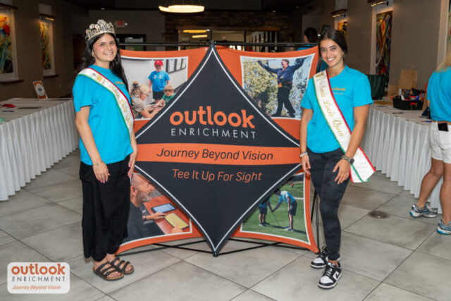 2 ladies from Santa Lucia smiling in front of the Tee It Up Fore Sight sign.