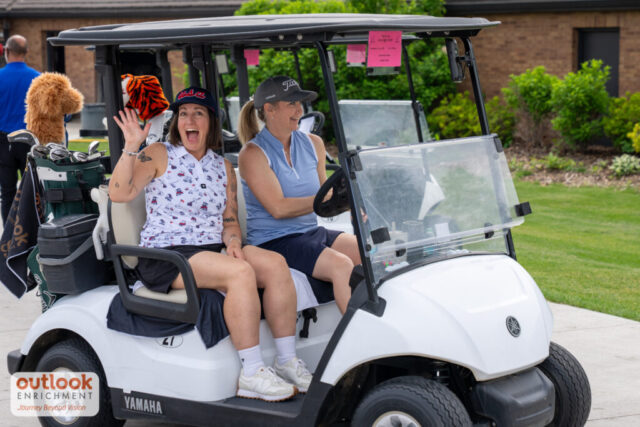 2 women smiling on their cart, one is waving.