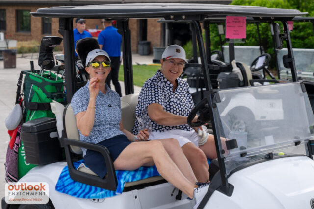 2 women smiling on their cart, one is waving.
