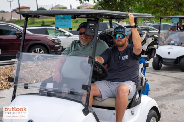 2 men smiling on their golf cart.