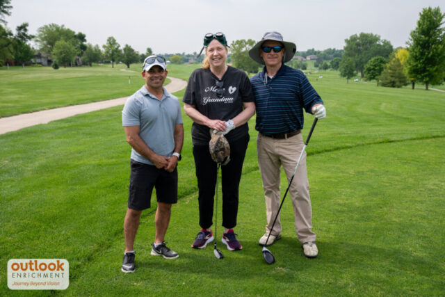 A woman smiling for a photo with two men on the course.