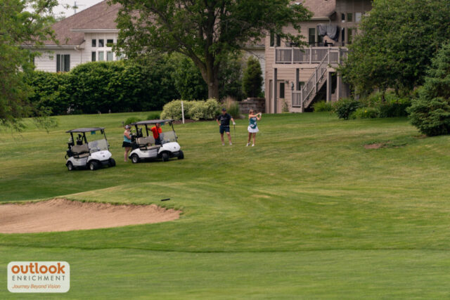 A zoomed out view of a woman swinging her club with her group watching.