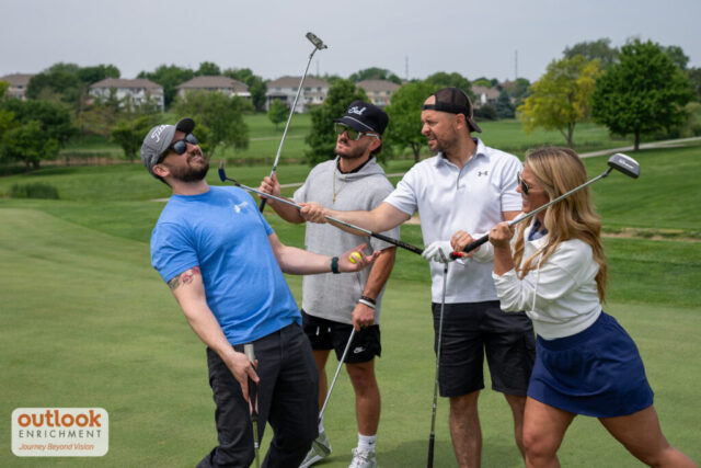 2 men and 1 lady pretending to hit a man with their clubs on the course.