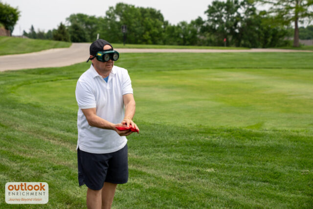 A man is getting ready to toss a cornhole bag with vision simulation goggles on.