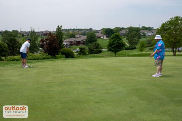 Male volunteer providing verbal guidance for a man putting with sleep shades on.