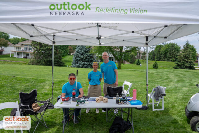 Volunteers smiling at their tent. 1 woman and 2 men.
