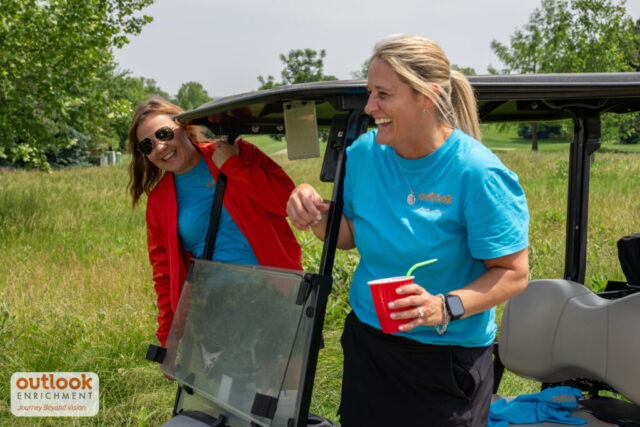 Two women smiling on a golf cart.