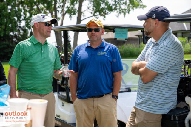 3 men chatting by a golf cart.