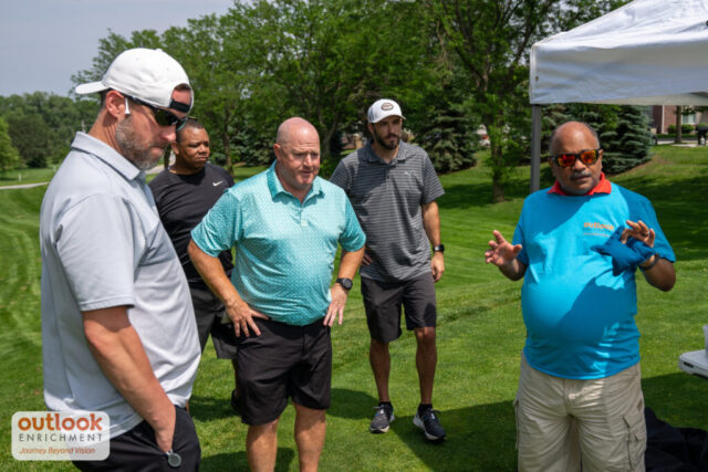 Group of men learning instructions for a hole game.