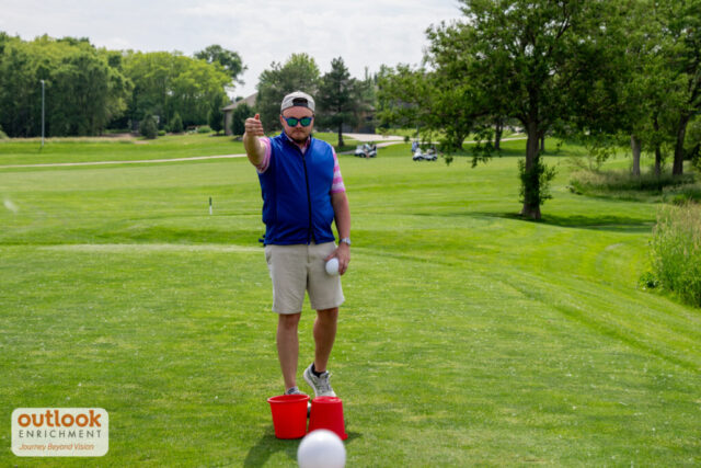 Man tossing a ball into a bucket for a hole challenge.