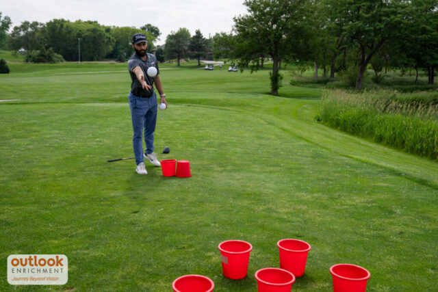 Man tossing a ball into a bucket for a hole challenge.
