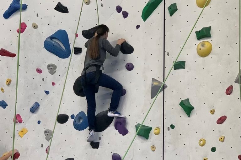 a teen scaling a wall with replicated rocks attached to it. The rocks are used as foot and hand grips while climbing the wall.