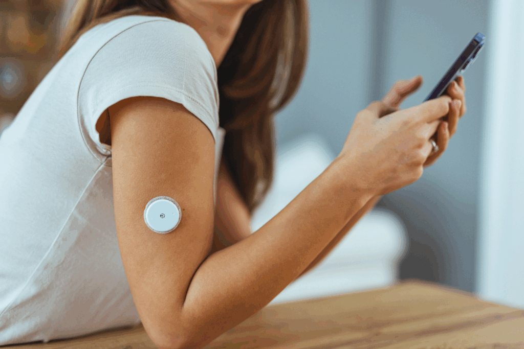 A woman wearing a continuous glucose monitor on her arm and holding up her phone.