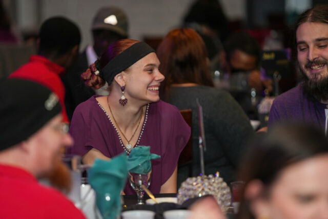 A woman looking outward smiling with the guests at the table.
