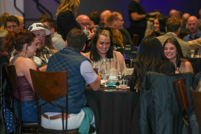 A group of four women and two men seated at a table smiling and laughing.