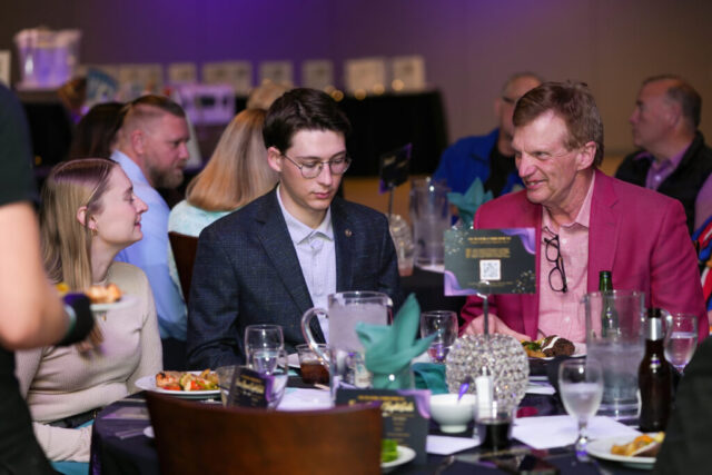 Two men and a woman talking at their table with dinner in front of them.