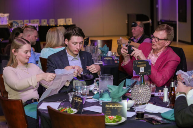 A man is taking a photo of a man and woman at this table as they get their bibs and sleep shades out.