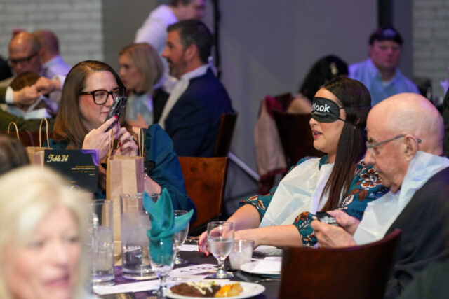 A woman is taking a photo of another woman wearing her sleep shades.