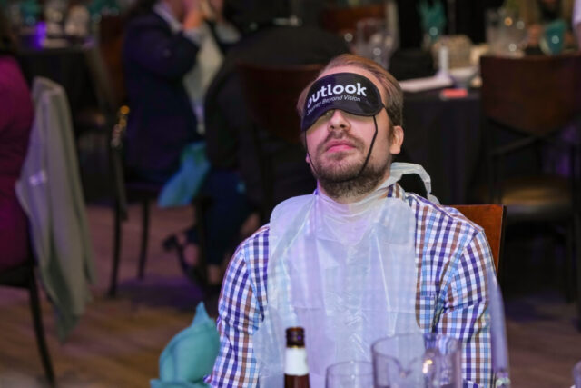 A man is wearing his sleep shades and bib.