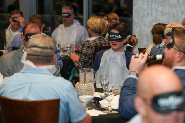 A table of men with their sleep shades on and bibs on.