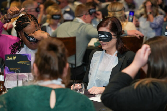 A with her sleep shades and bib on is next to another woman mid putting her sleep shades on.