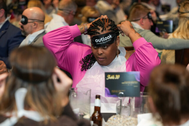 A woman wearing a bib is midway through putting her sleep shades on.