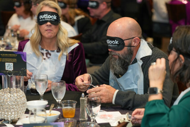 A man and woman wearing sleep shades and a bib are eating their dessert.