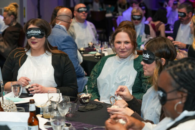 A table of women eating enjoying Dessert in the Dark. One is not wearing sleep shades and looking at the camera.