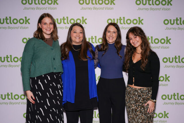Four women volunteers smiling in front of an Outlook backdrop.