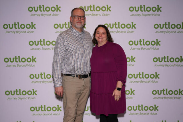 Steve and a woman smiling in front of an Outlook backdrop.