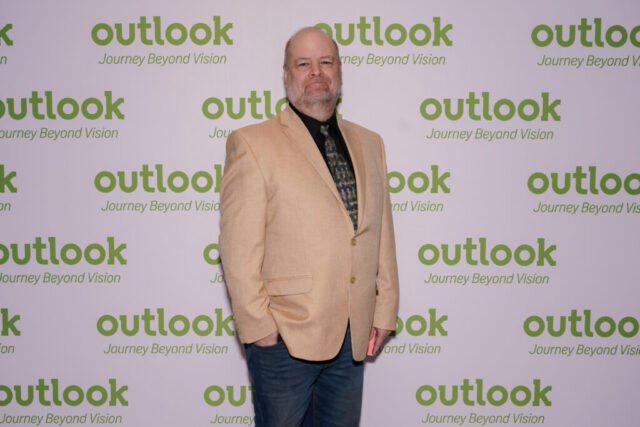 A man in front of an Outlook backdrop.