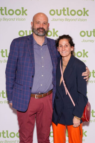 A man and woman smiling in front of an Outlook backdrop.