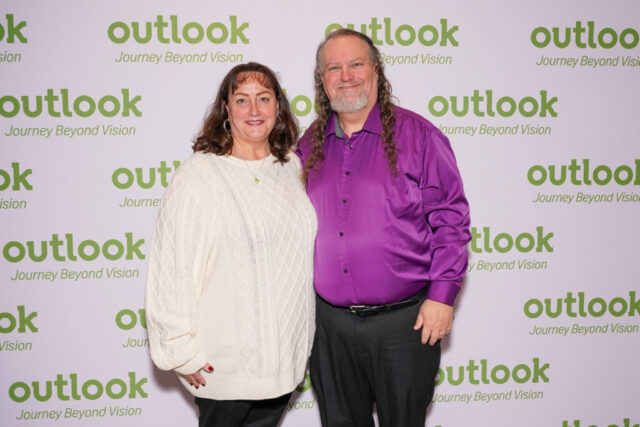 Karen and a male guest are smiling in front of an Outlook backdrop.